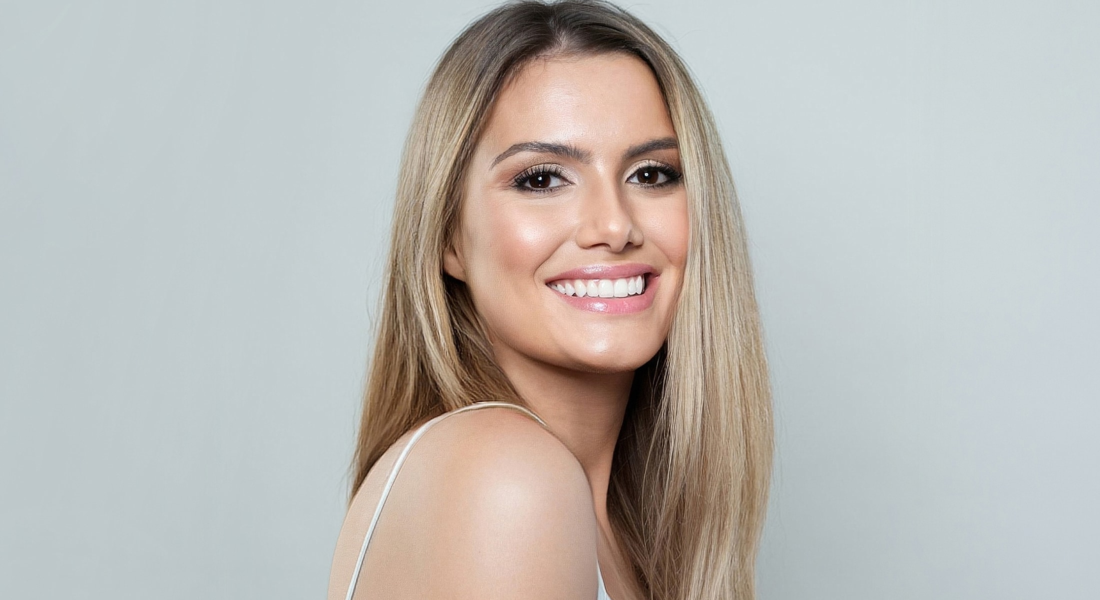 Smiling woman with long blonde hair against gray background.